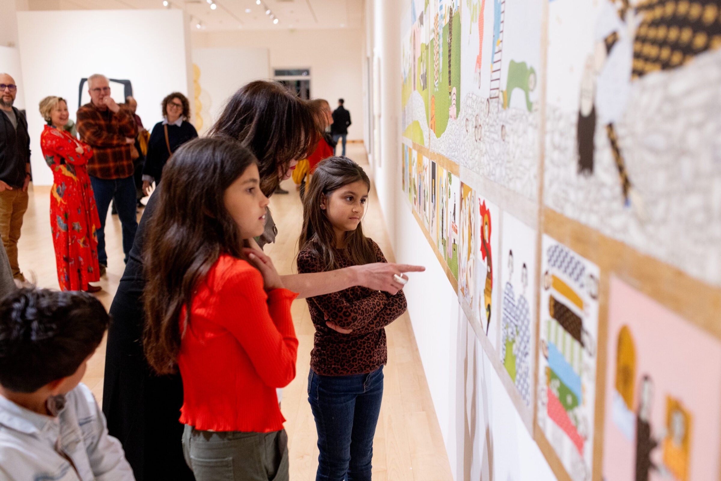An artist pointing at their artwork with two young children beside them.