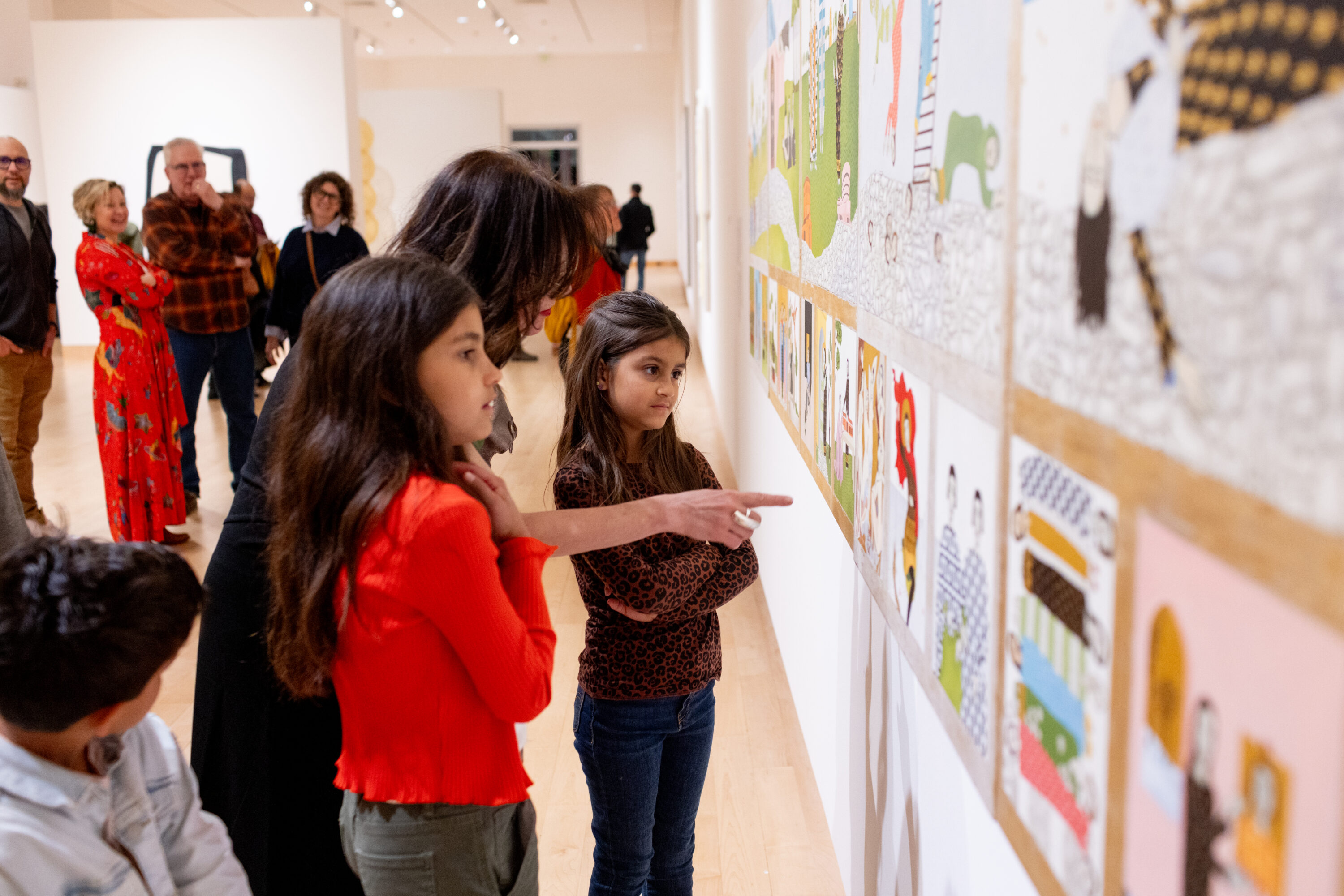 An artist pointing at their artwork with two young children beside them.
