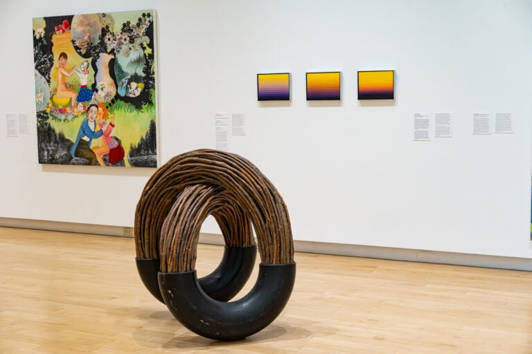 A gallery space with artwork on the wall and a wooden sculpture.