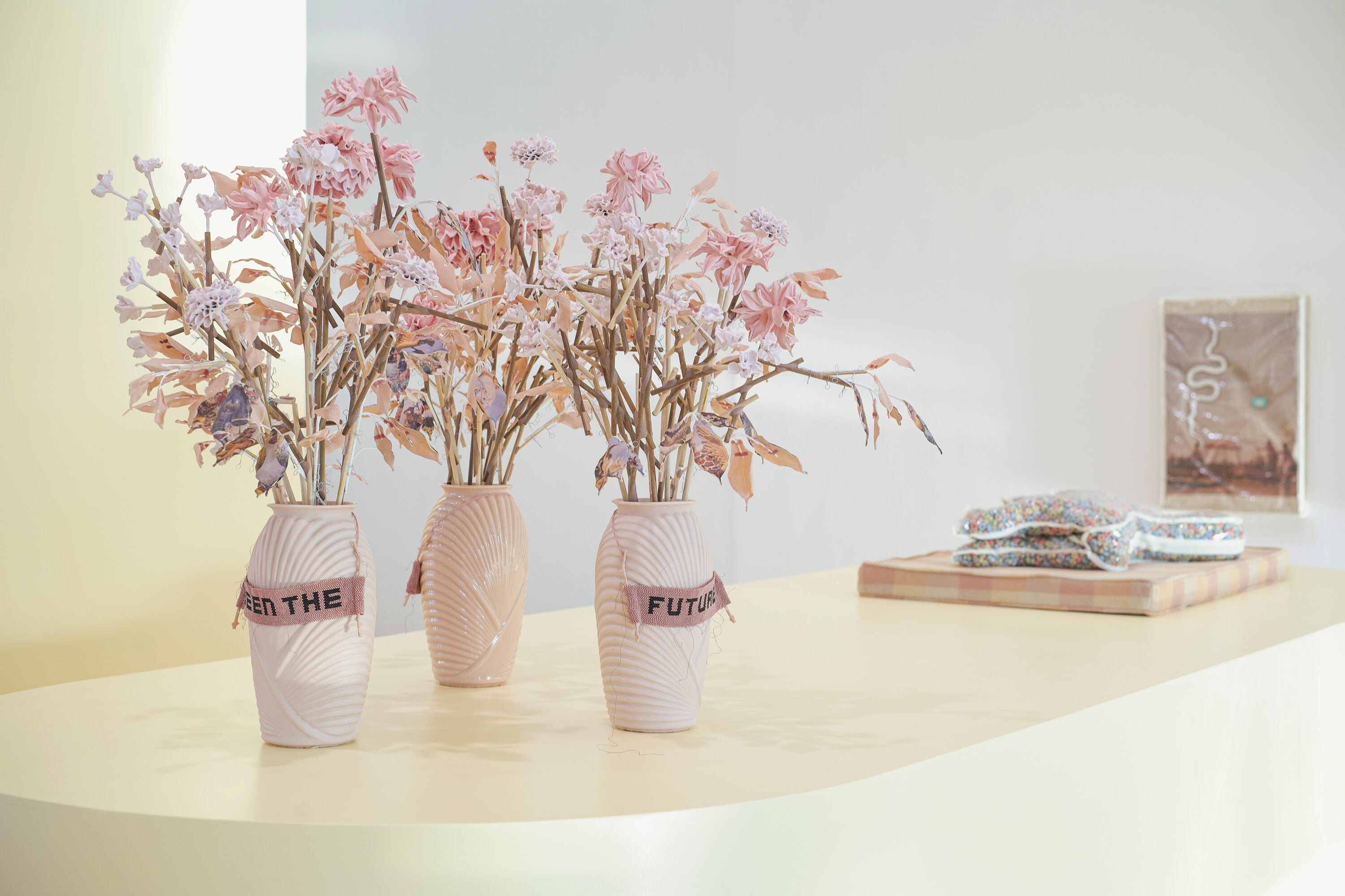Flowers in vases next to two plastic art works in a gallery space.