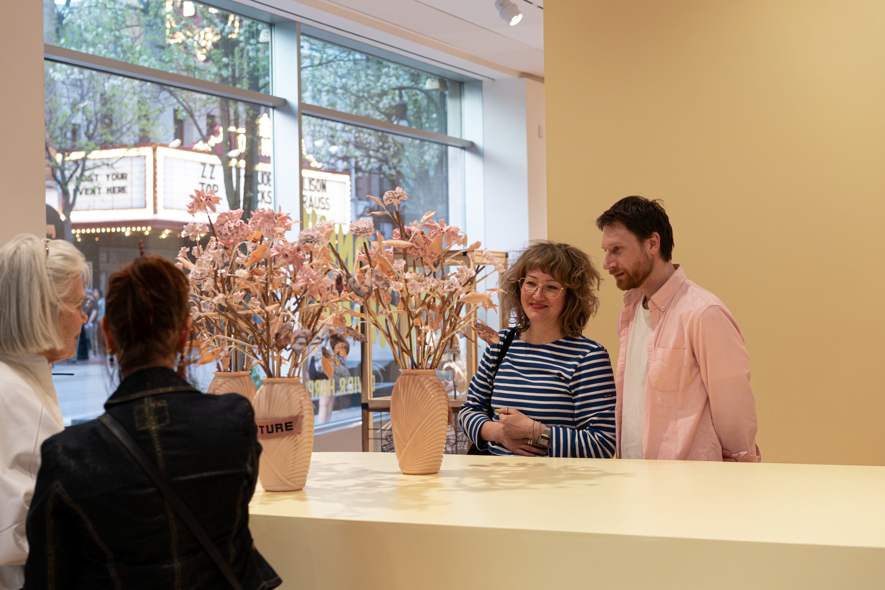 People looking at a pink flower bouquet in a gallery space with yellow walls. 