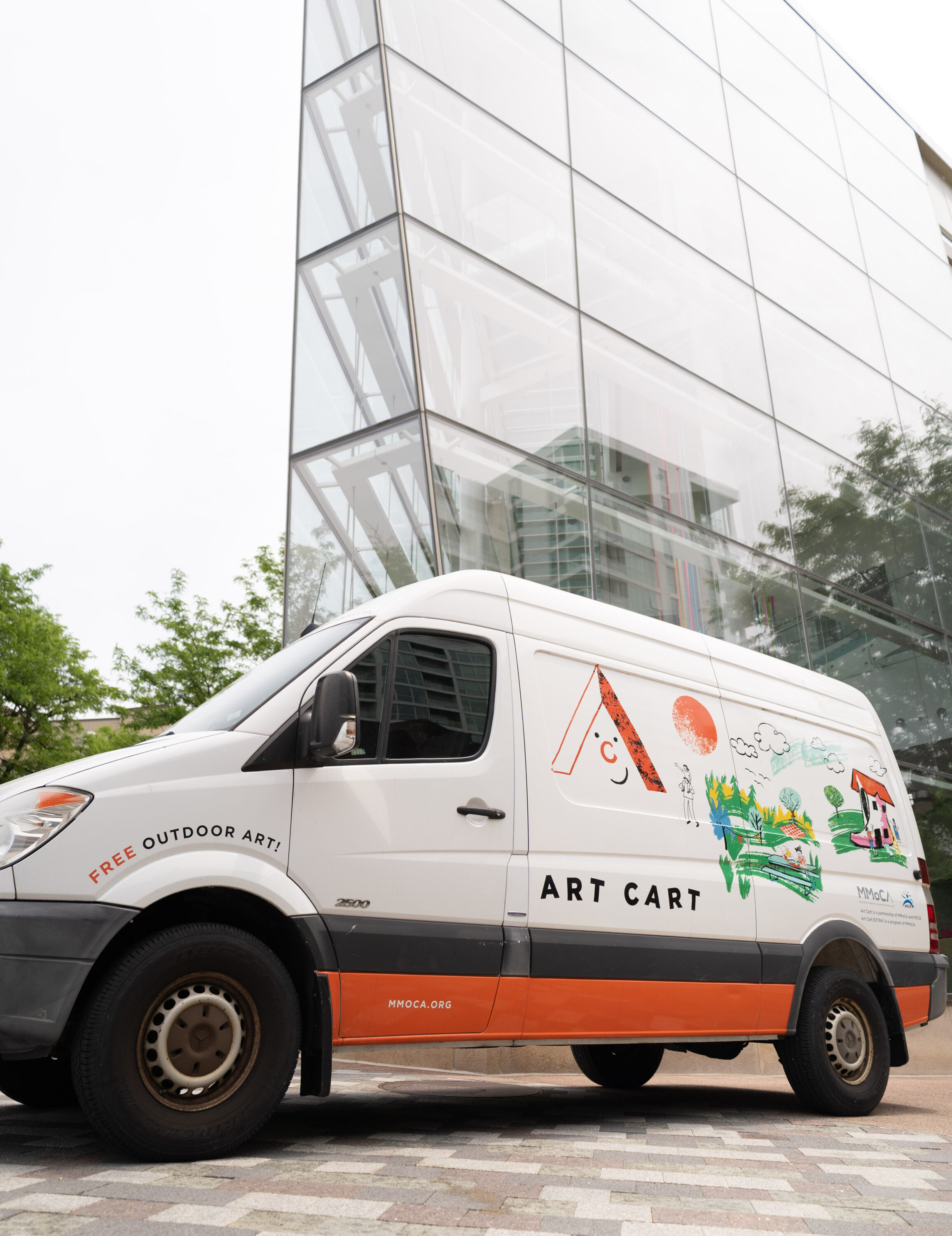 A white van with orange accents in front of a glass building.
