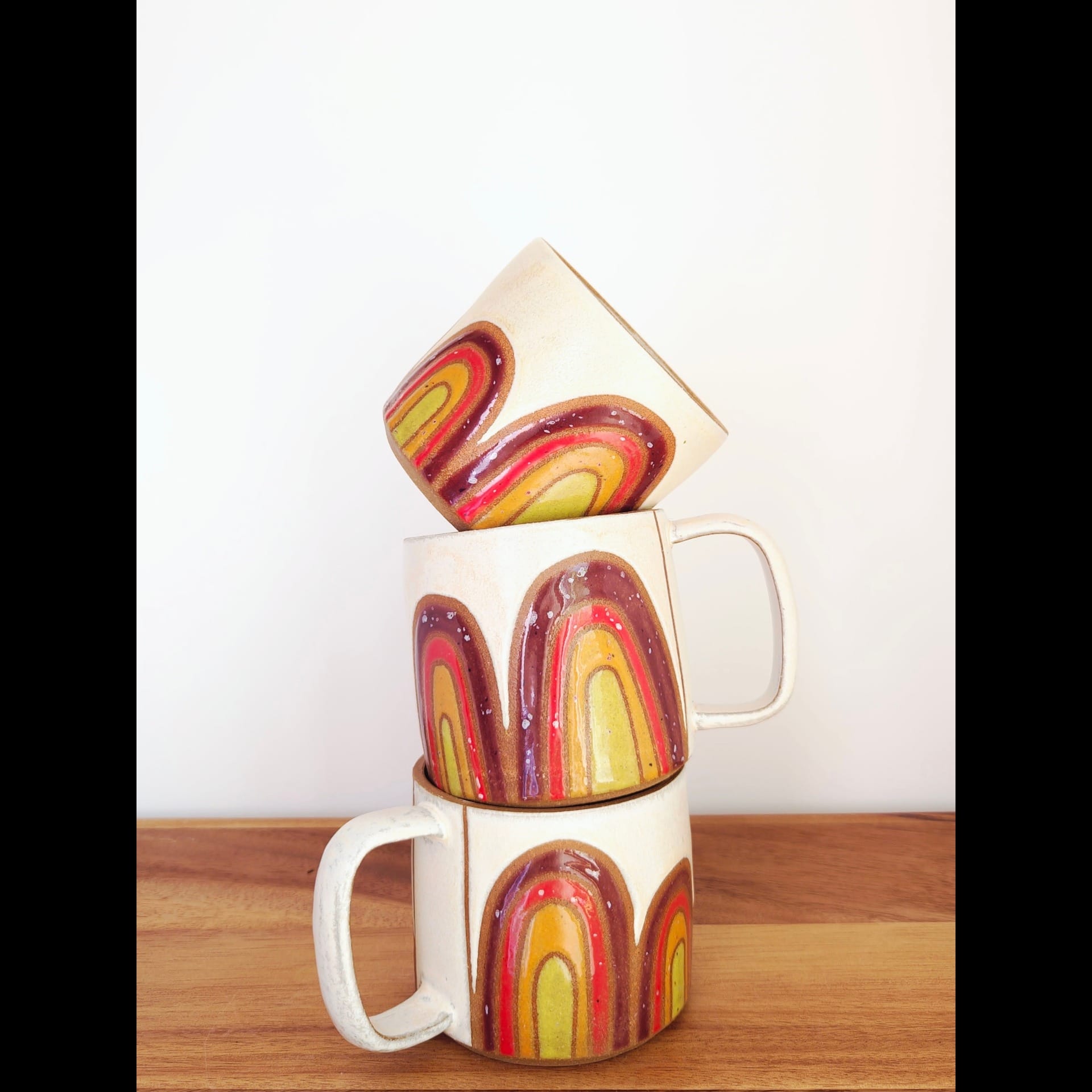 Three mugs stacked on top of one another with orange and yellow designs.