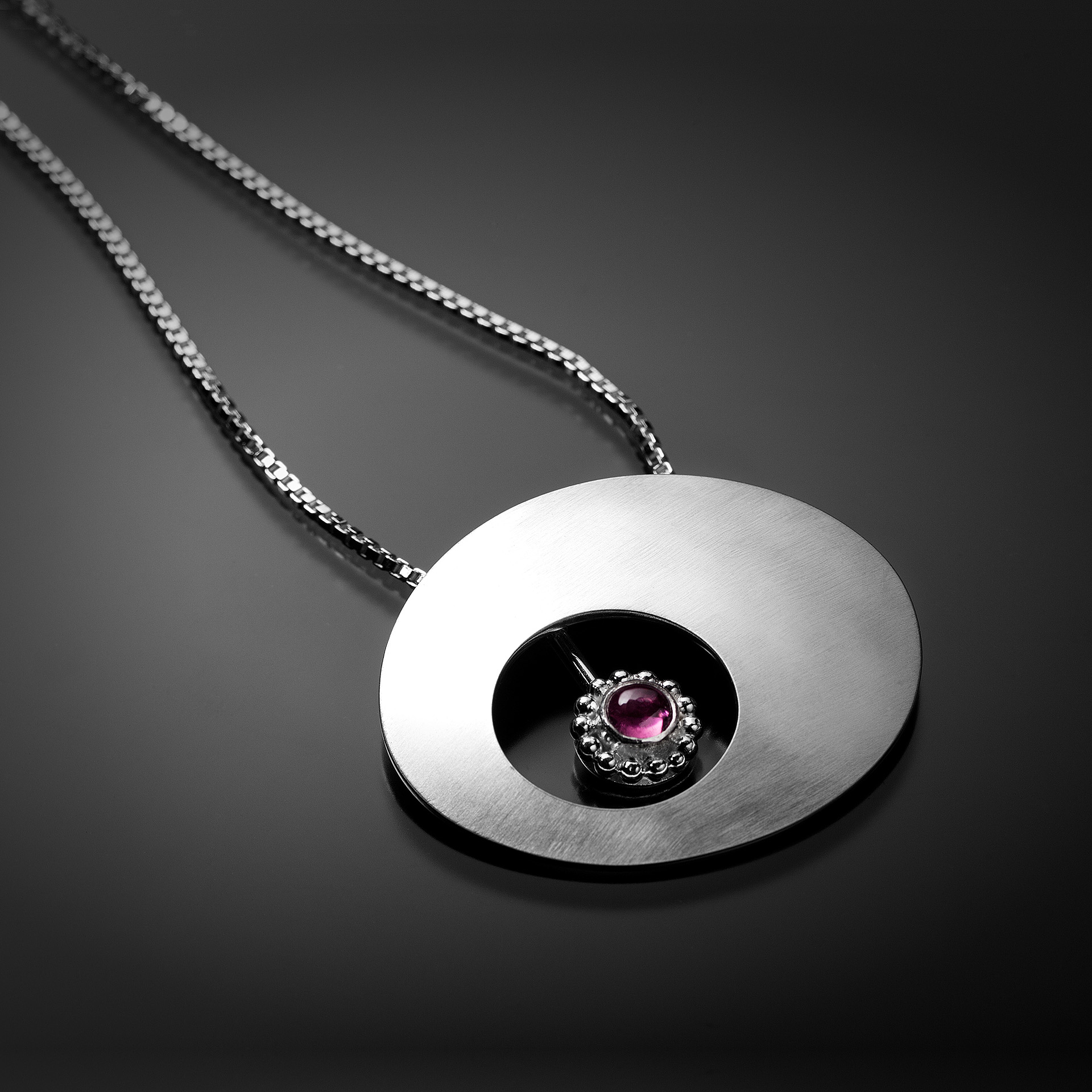A necklace with a silver pendant with a purple gem in the center.