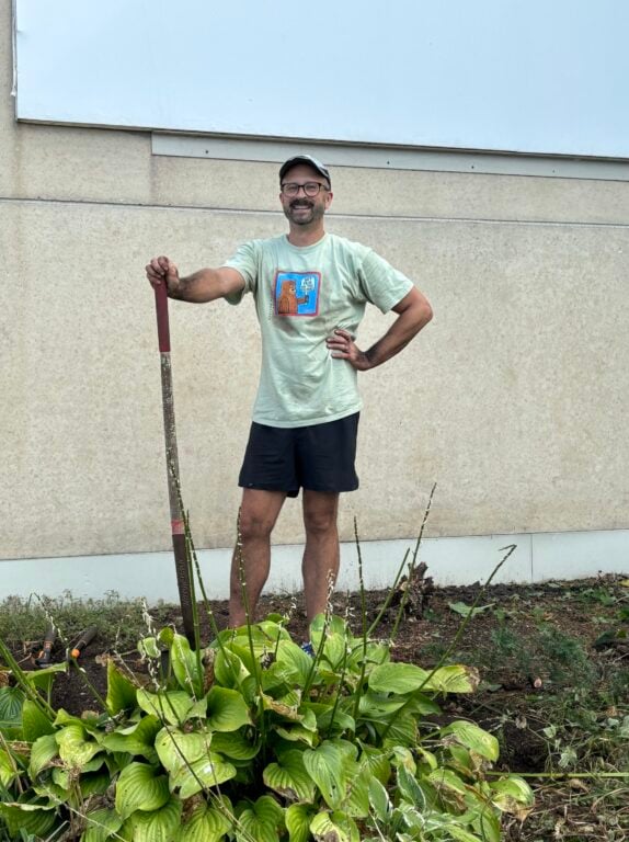 A man standing next to some plants with a shovel in hand.