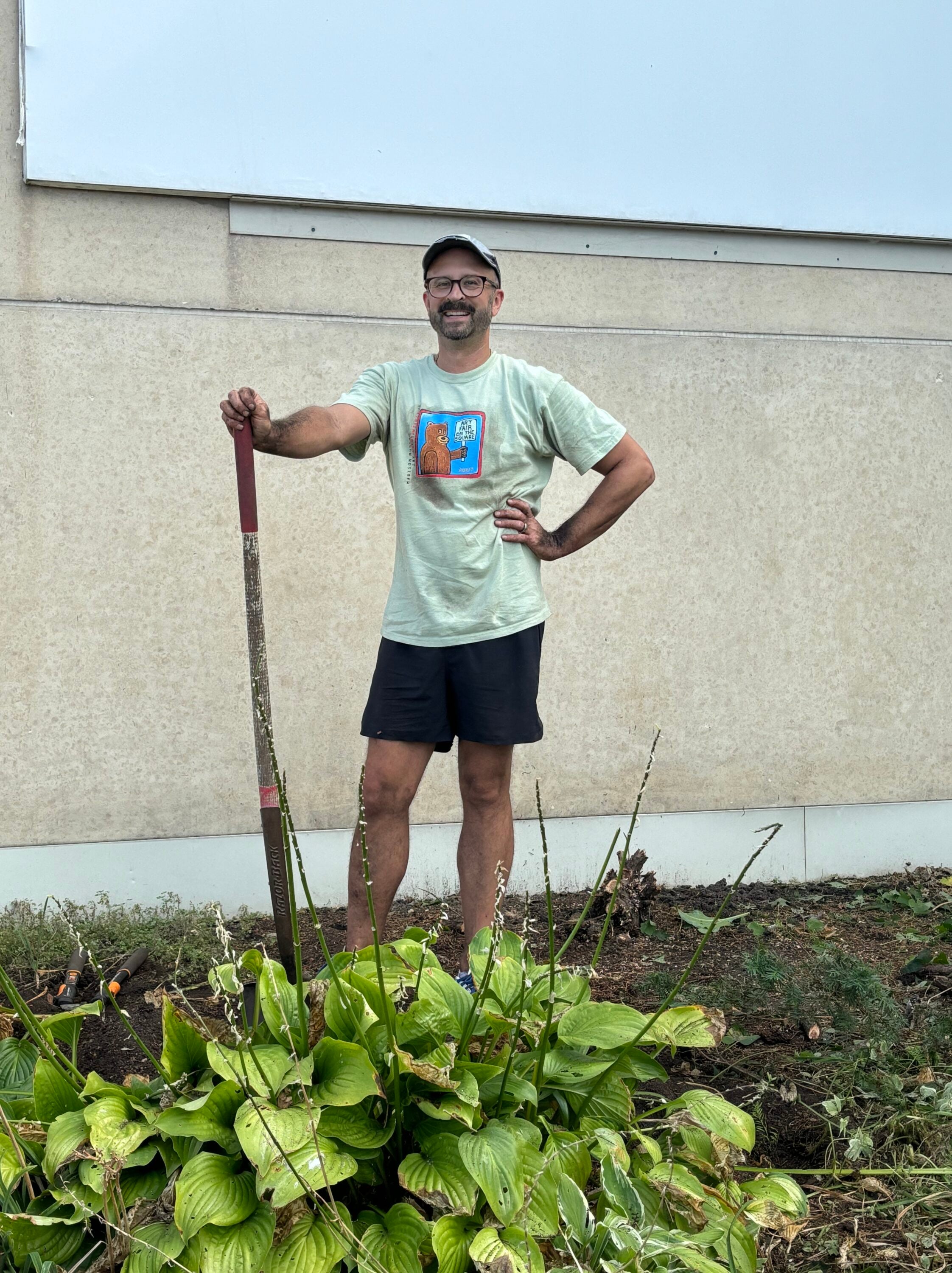 A man standing next to some plants with a shovel in hand.