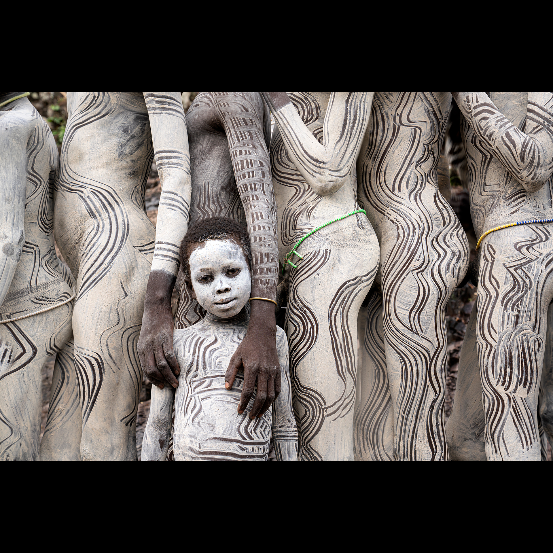 A group of people and a child painted with white tribal markings.
