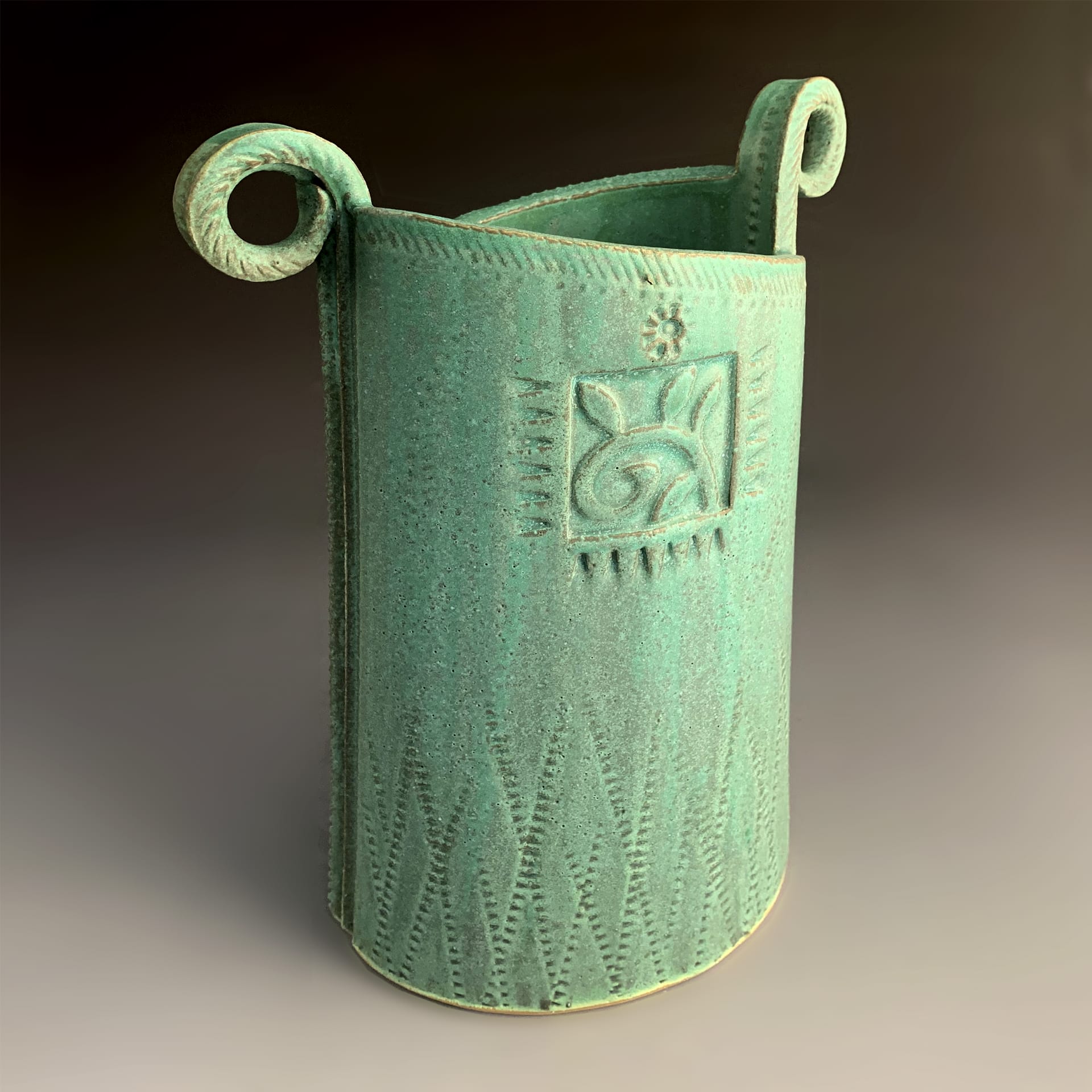 A teal vase with designs on it.