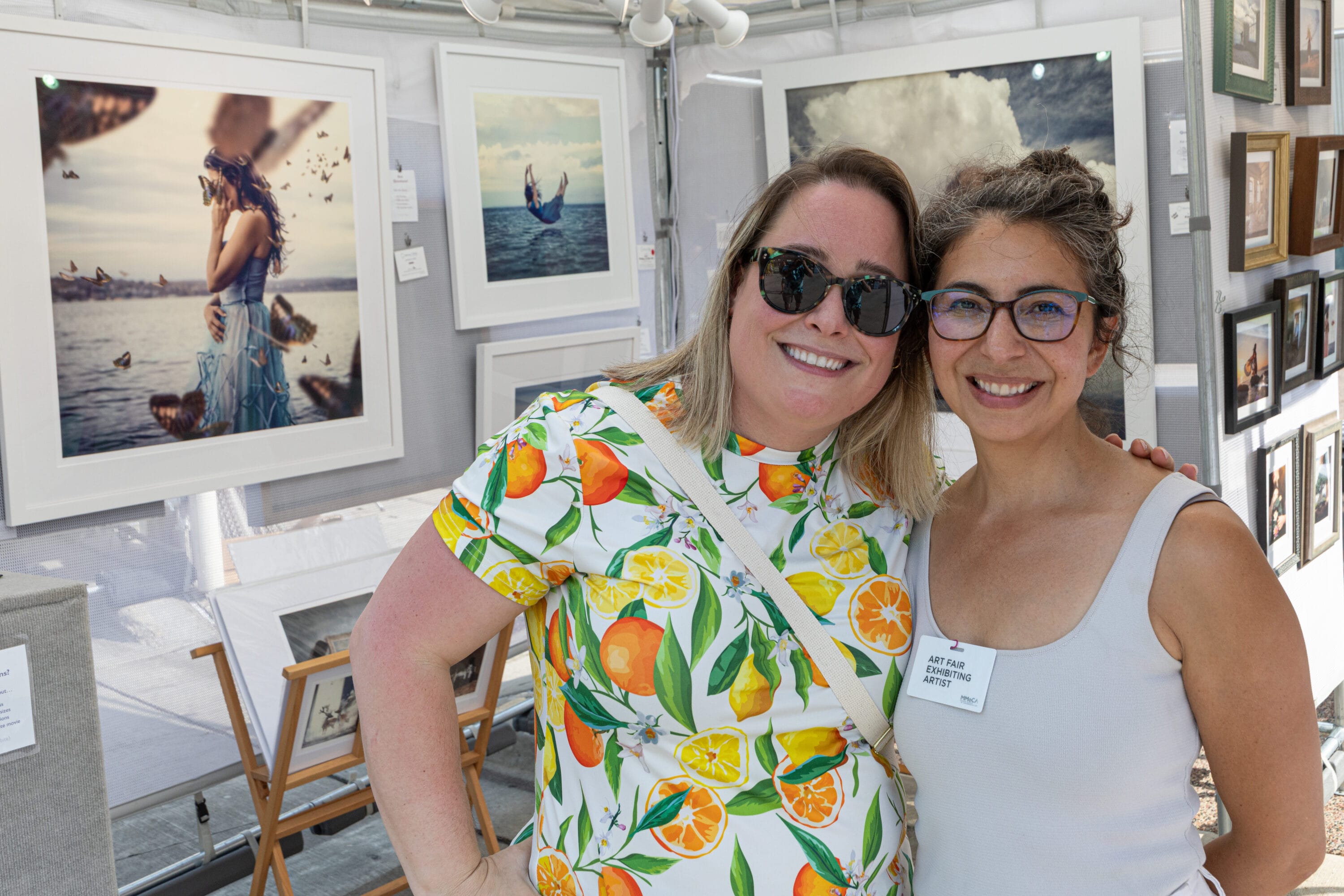 Two women side by side. One in a colorful floral print, the other with a "Participating Artist" name badge.