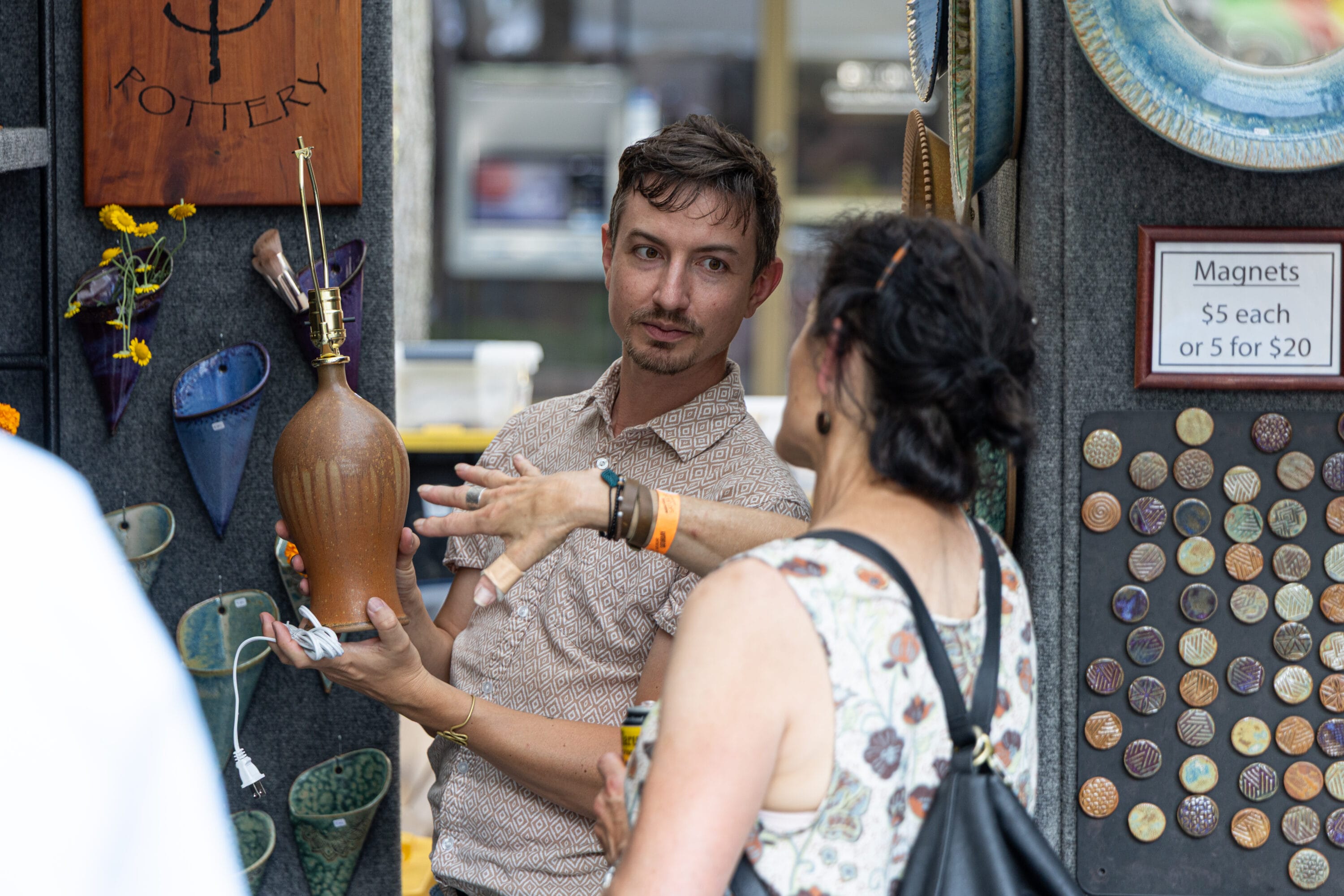 An artist holding their wares speaking with a visitor to Art Fair on the Square. 