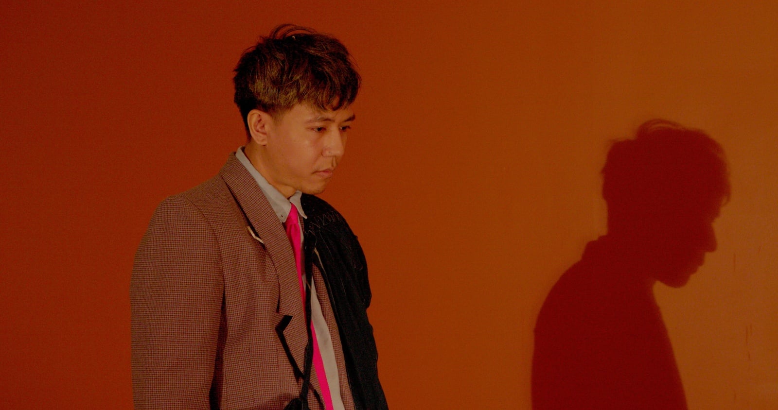 A person in a brown suit against an orange background.