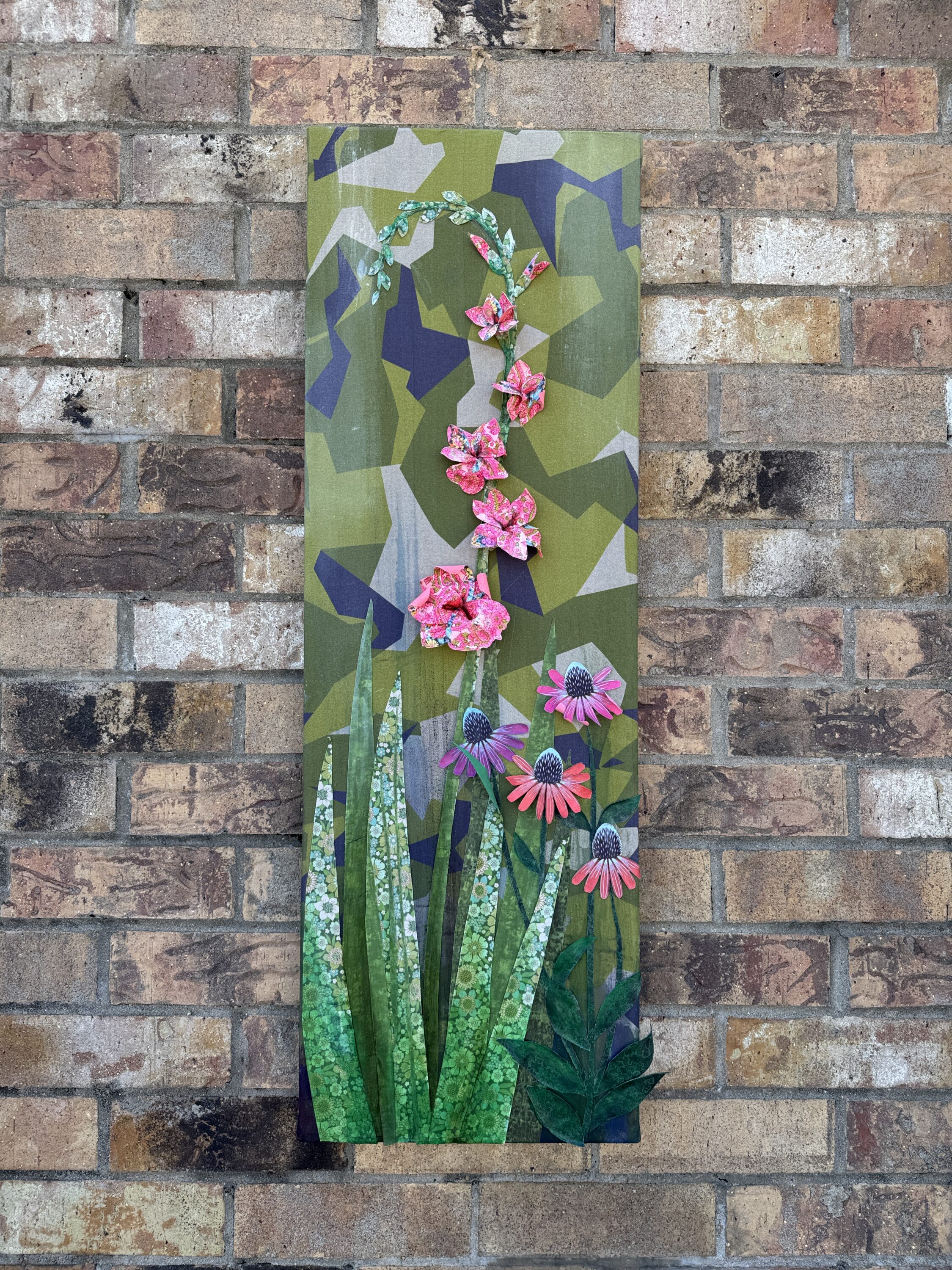 A painting of tall flowers against a brick wall. 